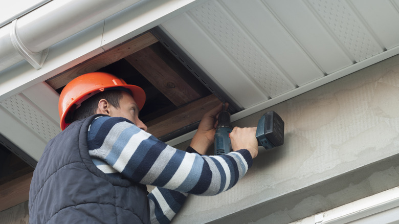 Man replacing soffit under a roof