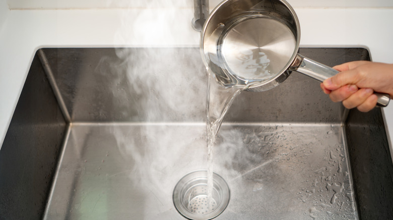 A person pouring boiling water into the sink to flush drain