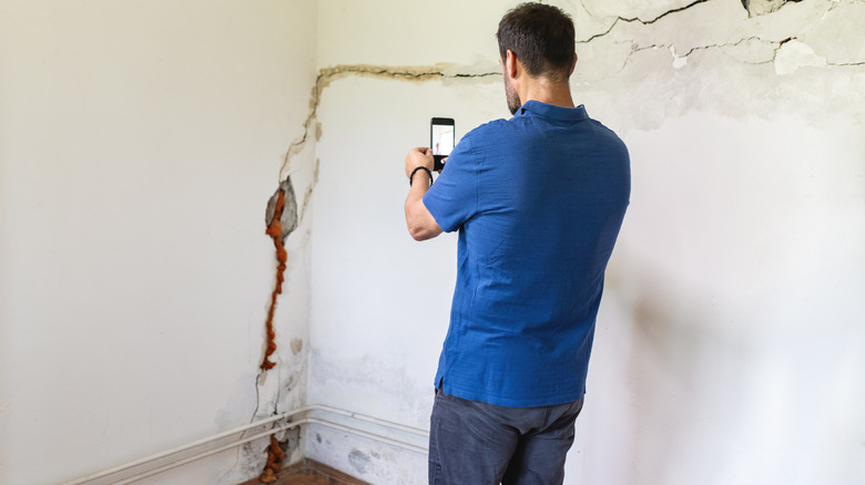Person standing near a damaged wall taking a photo