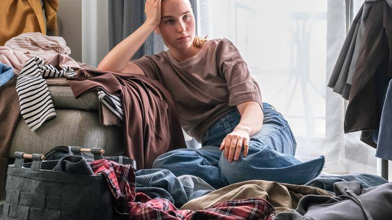 Sad woman surrounded by clothes on all sides
