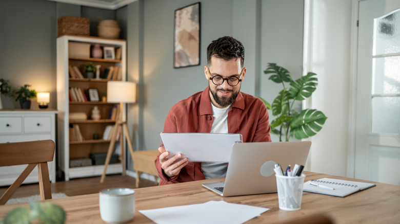 Man using laptop and looking at clipboard