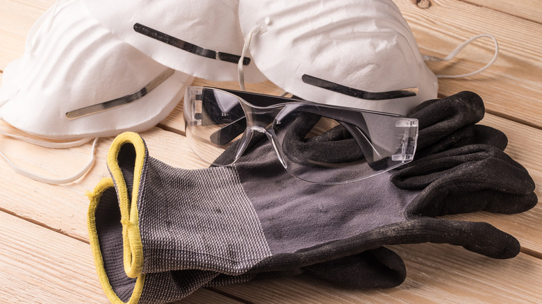 A collection of safety gloves, masks and goggles on a wooden table.