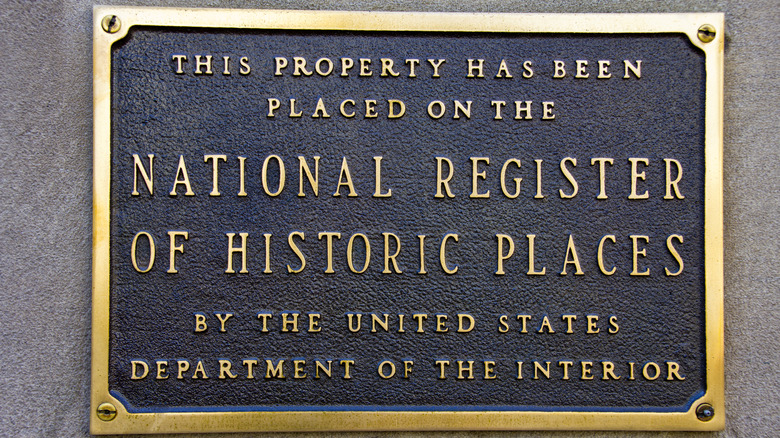 A shimmering gold plaque on the side of a grey building reads "This property has been placed on the National Register of Historic Places by the United States Department of the Interior"