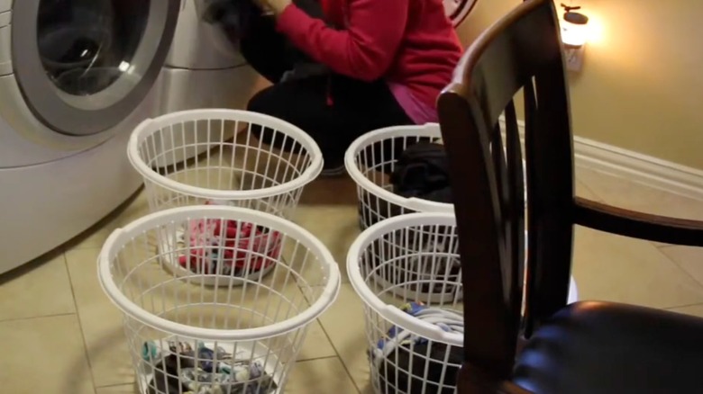 Four white Dollar Tree laundry baskets on the floor beside a person getting clothes out of the dryer.