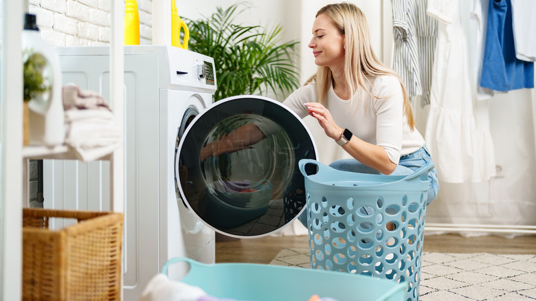 Woman taking clothing out of a washing machine to go in a blue laundry basket.