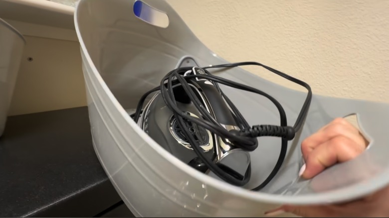 A gray tub used to store an iron in a laundry room.