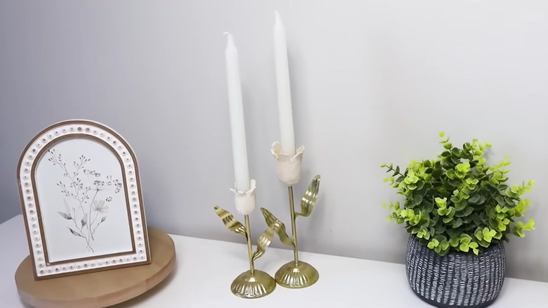 Two taper holders with clay flowers on top sitting next to other decor