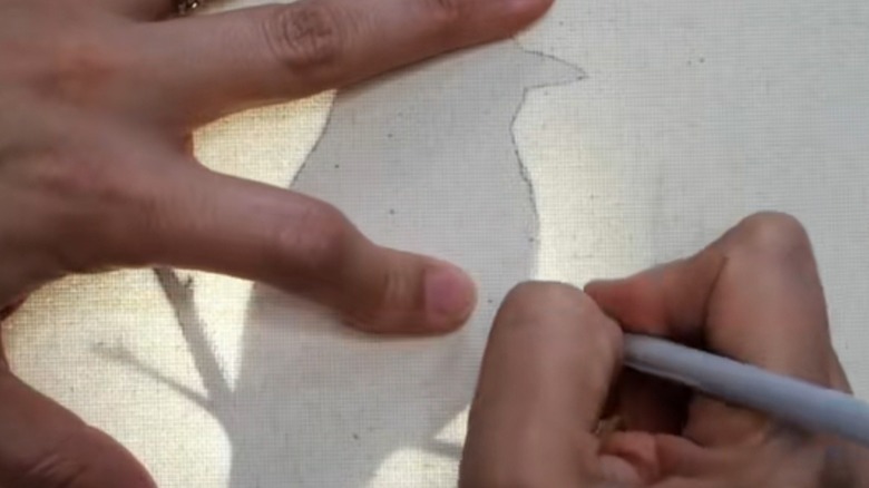 A pair of light-skinned hands trace a bird outline on a canvas.
