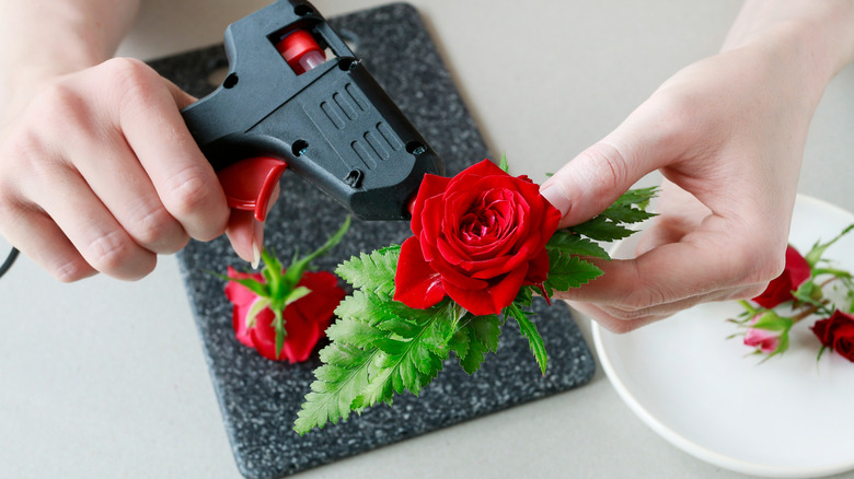 A woman hot gluing red roses to foam