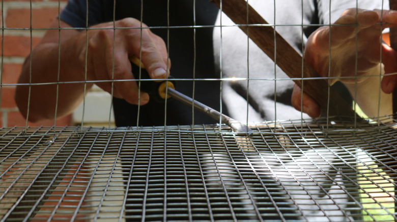 A man uses a flathead screw driver to bend wire rack