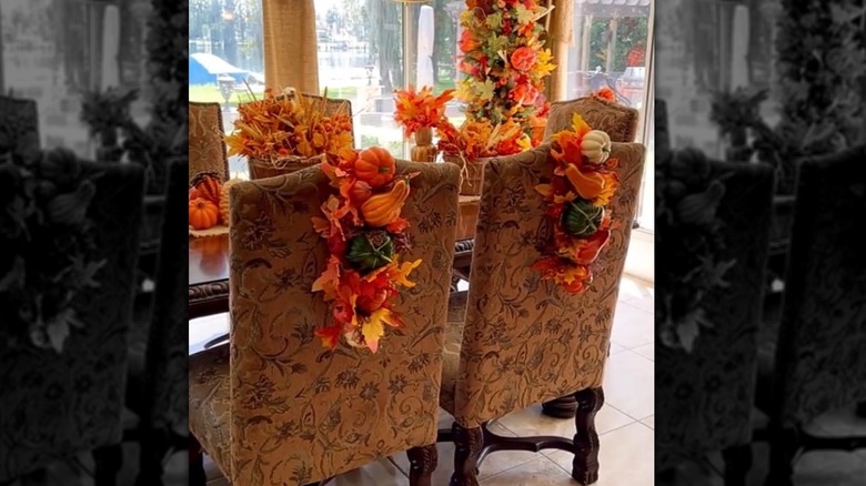 A dining room is adorned with fall decor including vertical wreaths hanging from chairs.