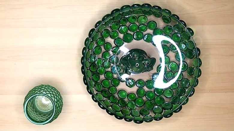 A small green vase next to a bowl covered in green glass gems on the underside with a frog figurine in the center