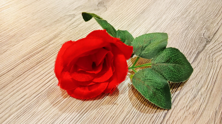 A red faux rose on a wood table