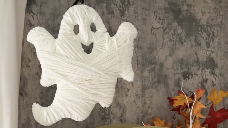 A wooden ghost cutout wrapped in white yarn