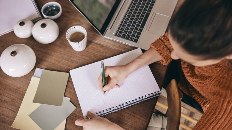 person writing in spiral notebook on desk
