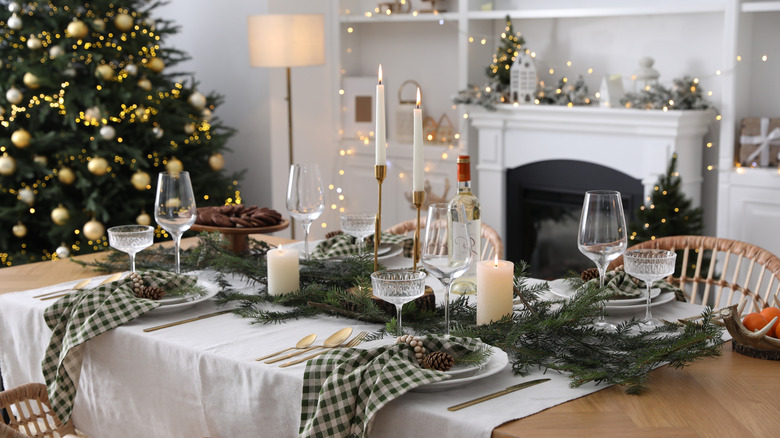 Christmas table laid out with pine cones, pine boughs, checkered napkins, crockery, glasses, and candles