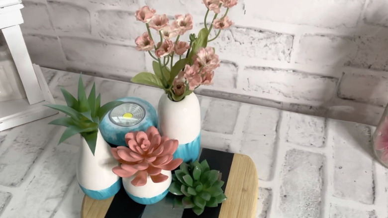 The push light sits behind three imitation plants in vases on a small cutting board.