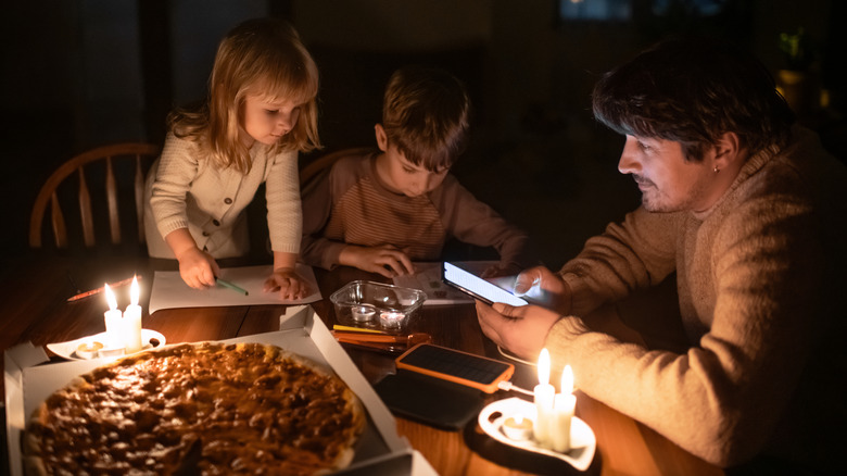 Kids and parent sit at a table in the dark surrounded by a pizza and some candles