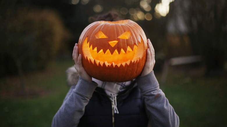 Person holding a lit Jack-o'-lantern to their face
