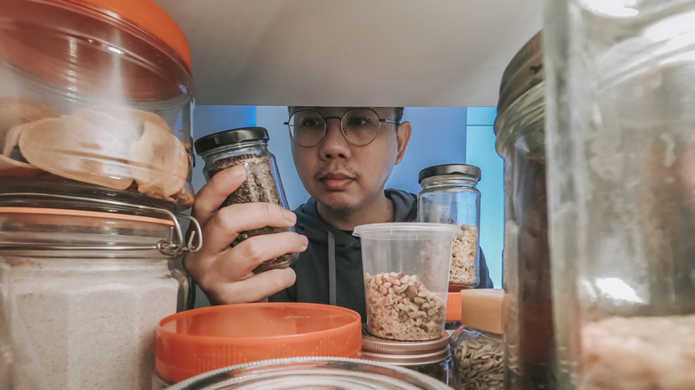 A person is grabbing a food item out of a kitchen cabinet
