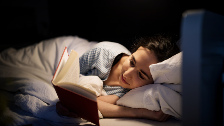 A woman is reading a book in a dark room with a small light shining