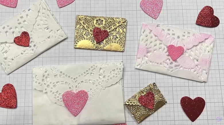 Multiple sizes and colors of paper doily envelopes with heart shapes in the background