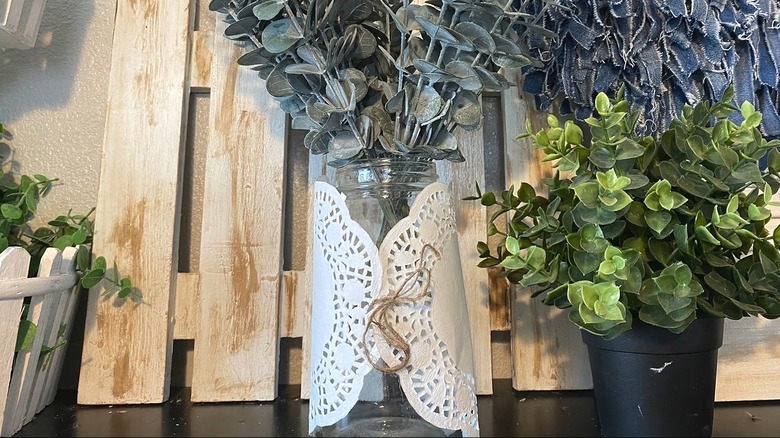 Mason jar with two paper doilies wrapped around it with twine to hold them in place and eucalyptus leaves inside