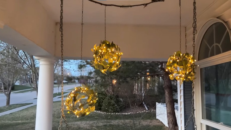 Three hanging lights with foliage over a wicker porch swing at dusk