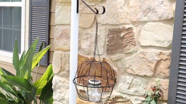 Glass jars with a solar light inside a cage made of hanging baksets on a pole near a stone wall
