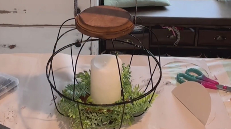 Candle inside a wire cage with foliage on a craft table