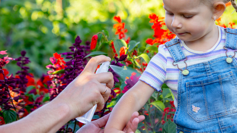 Man spraying a girl's arm with an insect repellent in a garden