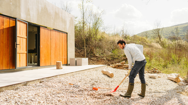 A man raking gravel outside of a home
