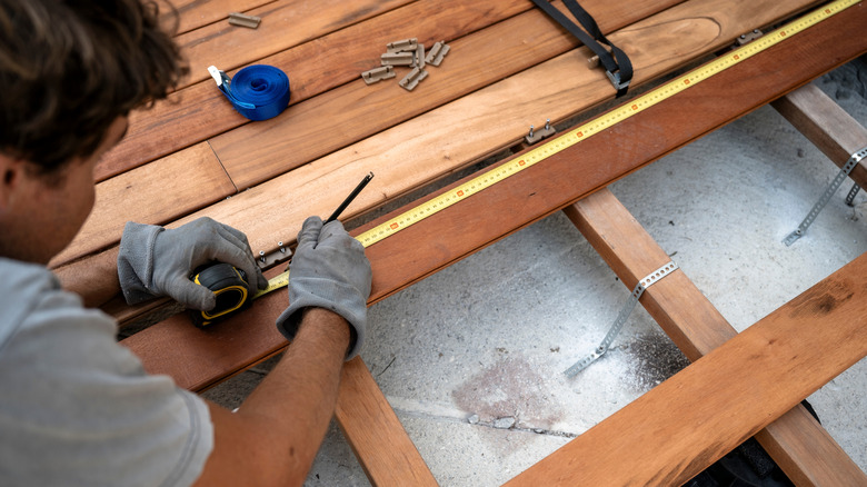 Person measuring wood decking boards with a tape measure while building a deck