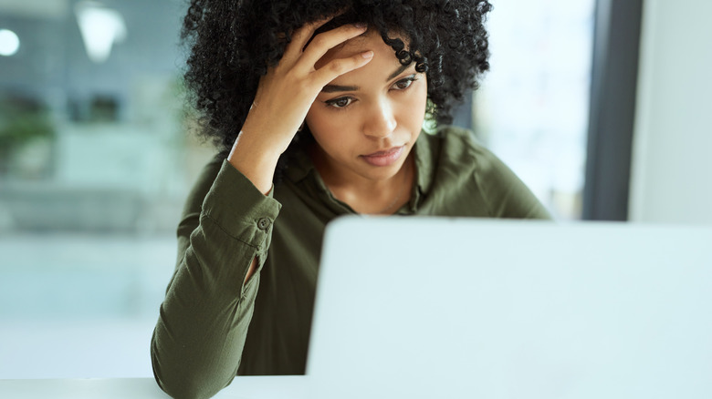 A medium dark-skinned woman looks exasperated in front of her computer.