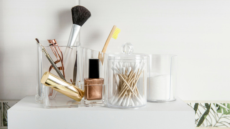 Makeup brushes and toiletries in plastic containers on a shelf in a bathroom