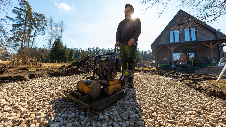 A man using a plate compactor on a gravel driveway.