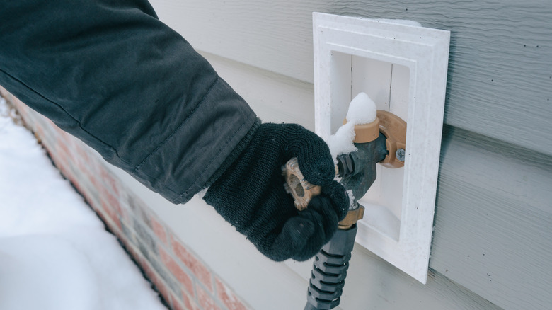 Gloved hand trying to turn the handle of an outdoor spigot covered in snow.