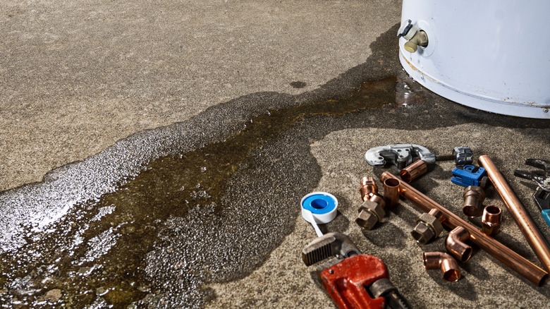 Water leaking from a hot water heater with tools on the concrete ground nearby