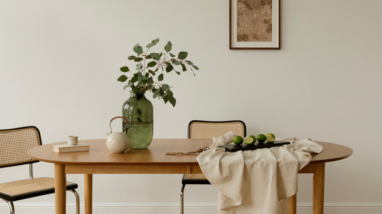 Two cane chairs sit next to a small round dining table with a green vase and some limes on it