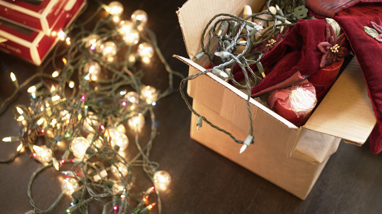Box of Christmas lights and other decor, a strand of lit white lights on the table