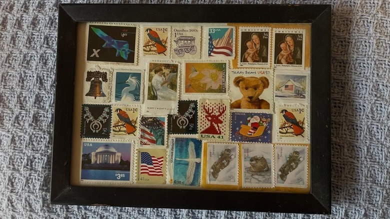 A collection of stamps framed as wall art sits on a gray crocheted blanket.