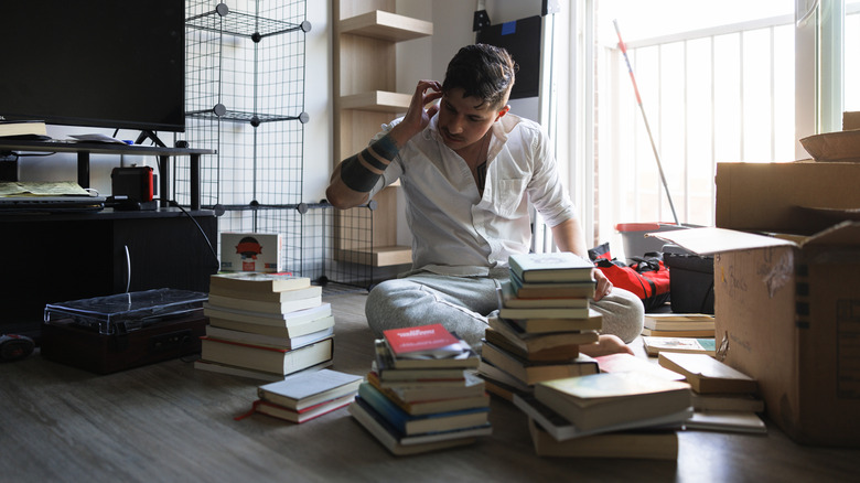 Man looks at the piles of old books around him, wondering what to do with them.