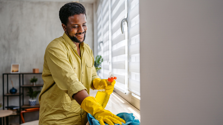 A man smiles as he wipes a window sill in his apartment