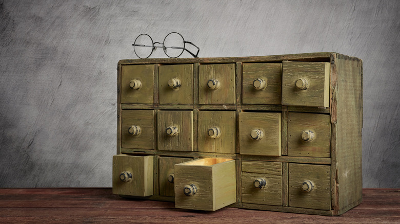 An old wooden apothecary cabinet with a set of glasses on top and one drawer pulled open.