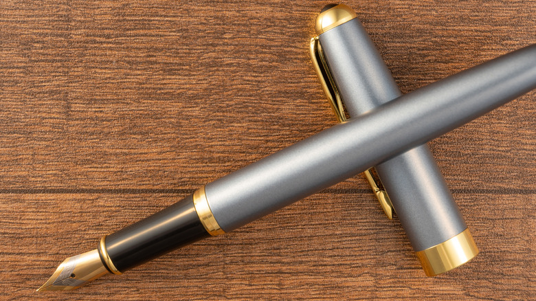 A beautiful gray and gold fountain pen with its lid off sits on a wooden tabletop.