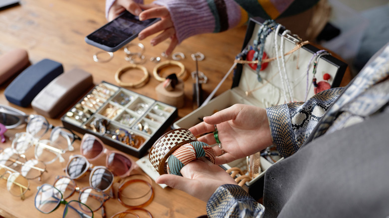 A woman holds vintage bracelets in her hands above a pile of secondhand accessories.