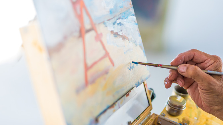 An artist signs their painting with a paintbrush.