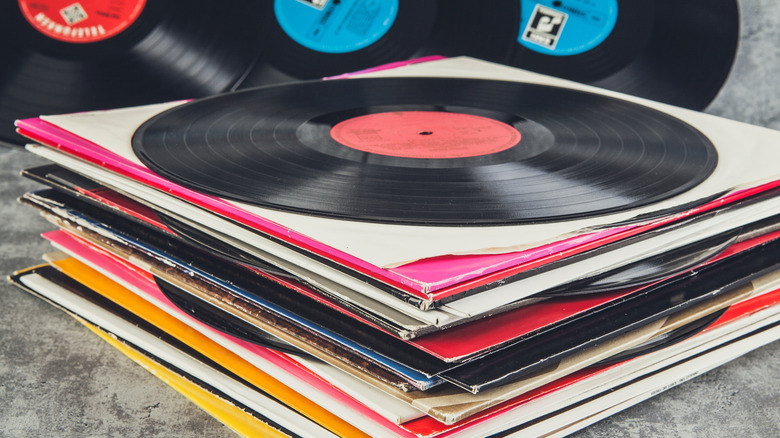 A stack of vintage vinyl records on a table with some un-sleeved records leaning on the wall behind it.