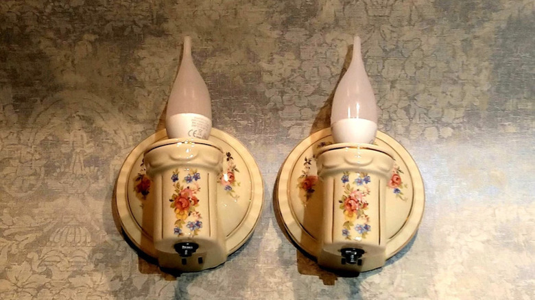 A pair of floral 1930s Porcelier sconces lying on a antique-patterned tabletop.