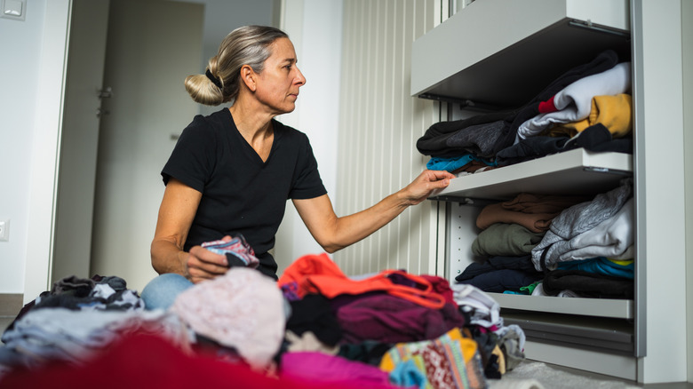 A person sits on the floor and attempts to organize messy closet shelves without dividers